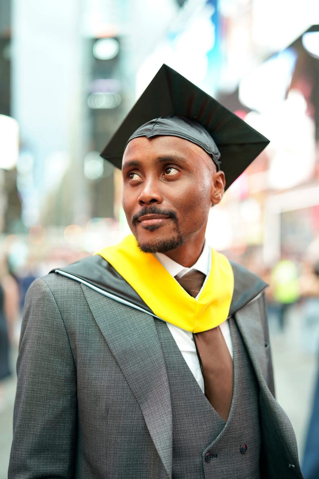 Emmanuel Olimi Kasigazi in graduation regalia in Times Square, New York